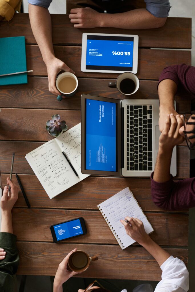 Group of coworkers discussing business strategies with laptops and tablets in a modern office setting.